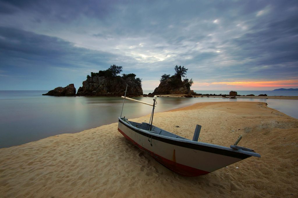 Peaceful beach scene with a boat, calm waters, and a vibrant sunset sky.